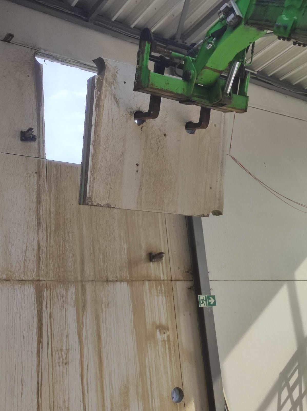 Ausgesägter Betonblock hängt an den Gabeln eines grünen Teleskopladers, darüber die neue Öffnung in der Wand