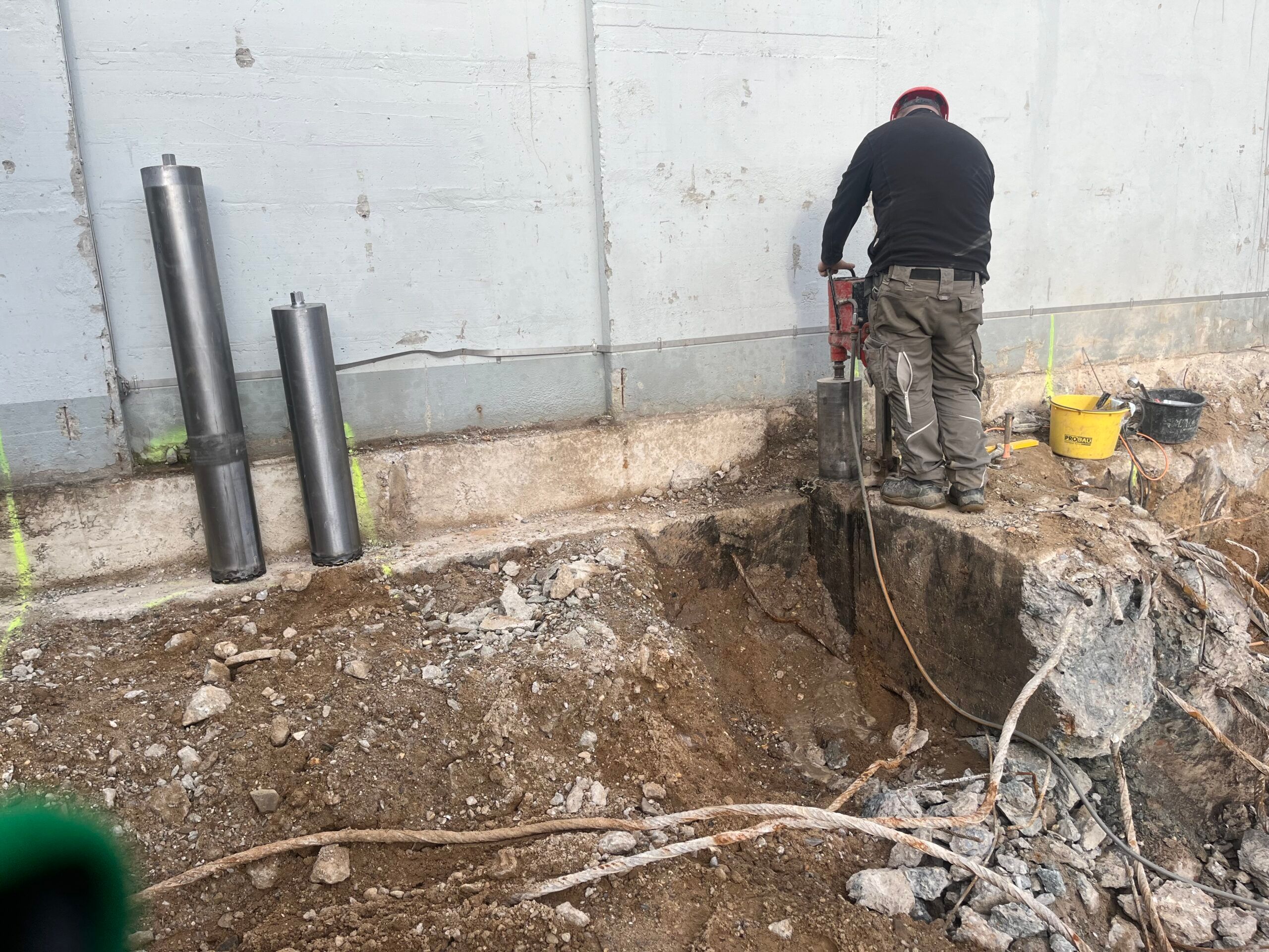 Kernbohrgerät auf dem Ständer vor einer Betonwand, daneben lehnen zwei große Bohrkronen