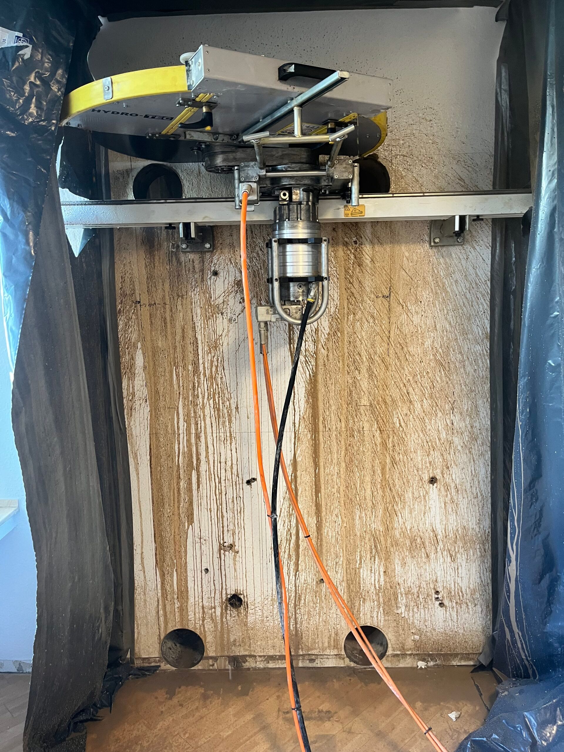 Wandsäge auf einer Schiene an einer Betonwand, unten zwei runde Eckbohrungen, ringsum Schutzfolie